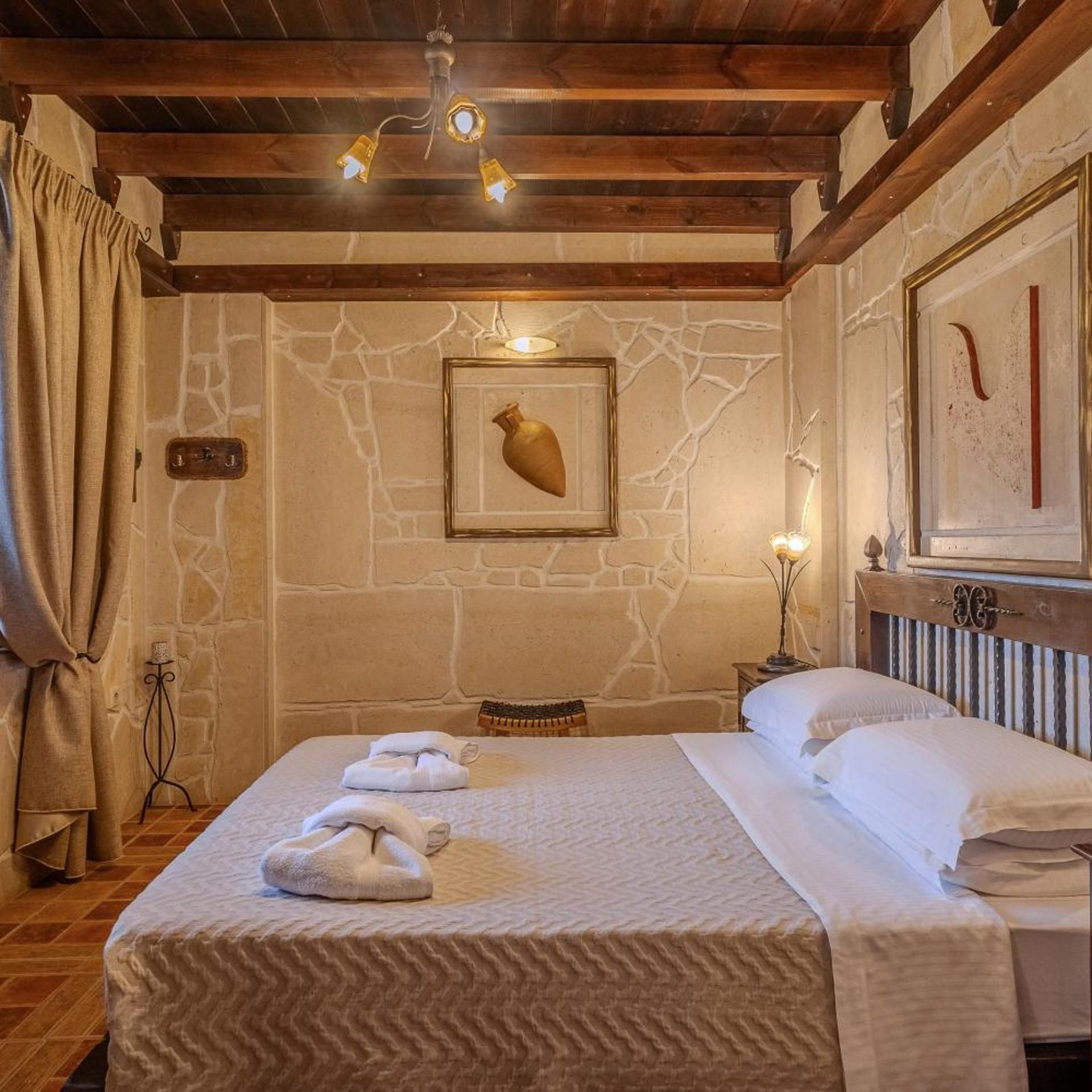 A hotel room with a stone wall, a bed with towels, a wooden ceiling, and a framed picture on the wall.