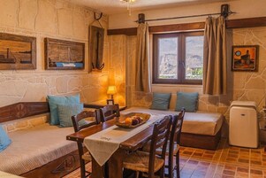 Una habitación acogedora con pared de piedra, muebles de madera, una mesa de comedor con fruta y una ventana con cortinas.