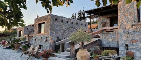 A stone building with a staircase leading to a covered area, surrounded by potted plants and outdoor seating.