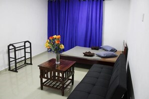 Ein Zimmer mit einem Bett, einer Couch, einem kleinen Tisch mit Blumenvase und einem schwarzen Metallregal.