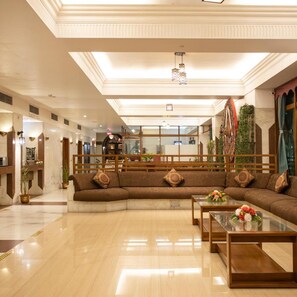 A spacious lobby with a large brown sofa, a wooden coffee table, and a reception desk. - OYO Premium Paltan Bazar (Guwahati)