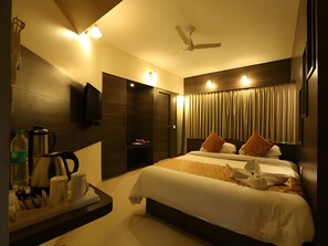 A hotel room with a bed, a flat-screen TV, a ceiling fan, and a minibar. - OYO Premium Paltan Bazar (Guwahati)