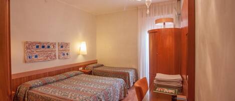 A hotel room with two beds, a wooden wardrobe, a glass table, and a chandelier.