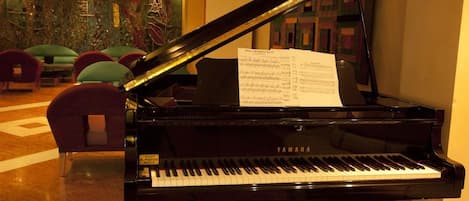 A grand piano with sheet music in a lobby area with seating and a decorative wall.