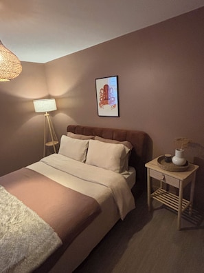 Ein Schlafzimmer mit einem Bett, einem Nachttisch, einer Lampe und einem Wandbild.