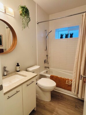 Ein Badezimmer mit Waschbecken, Toilette, Dusche und einem Fenster mit Pflanzen.