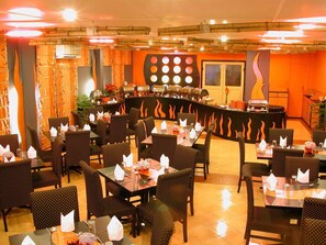Un restaurant doté de plusieurs tables et chaises, d’un espace buffet et d’un comptoir où sont présentés les plats.