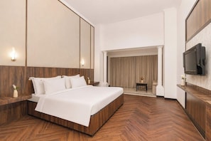 Une chambre d’hôtel moderne avec un grand lit, un plancher en bois, une télévision et une vue sur le hall d’entrée.
