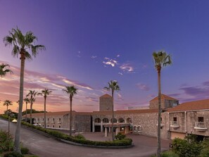 A courtyard with palm trees, a central building with arches, and a clear sky. - Altia Toba (Toba)