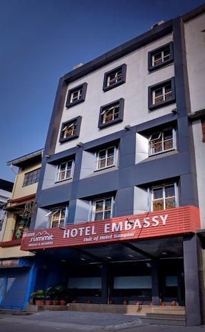 Un edificio a più piani con un cartello rosso ben visibile per 'Hotel Embassy', che indica che fa parte di Hotel Gangaur.
