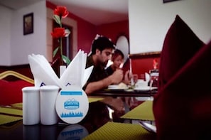 Una mesa de comedor con una botella de Mountain Dew, un porta servilletas blanco y un florero rojo.