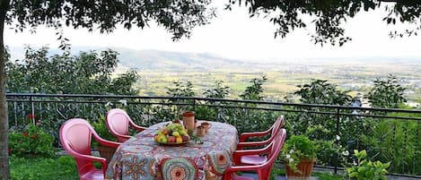 An outdoor dining area with a table set for four, surrounded by red chairs, with a view of a landscape in the background.