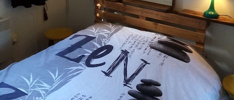 Un lit recouvert d’un drap blanc orné de motifs noirs et d’illustrations de groupes de rock, flanqué de deux lampes vertes posées sur des tables de chevet en bois, et un tableau encadré accroché au mur.