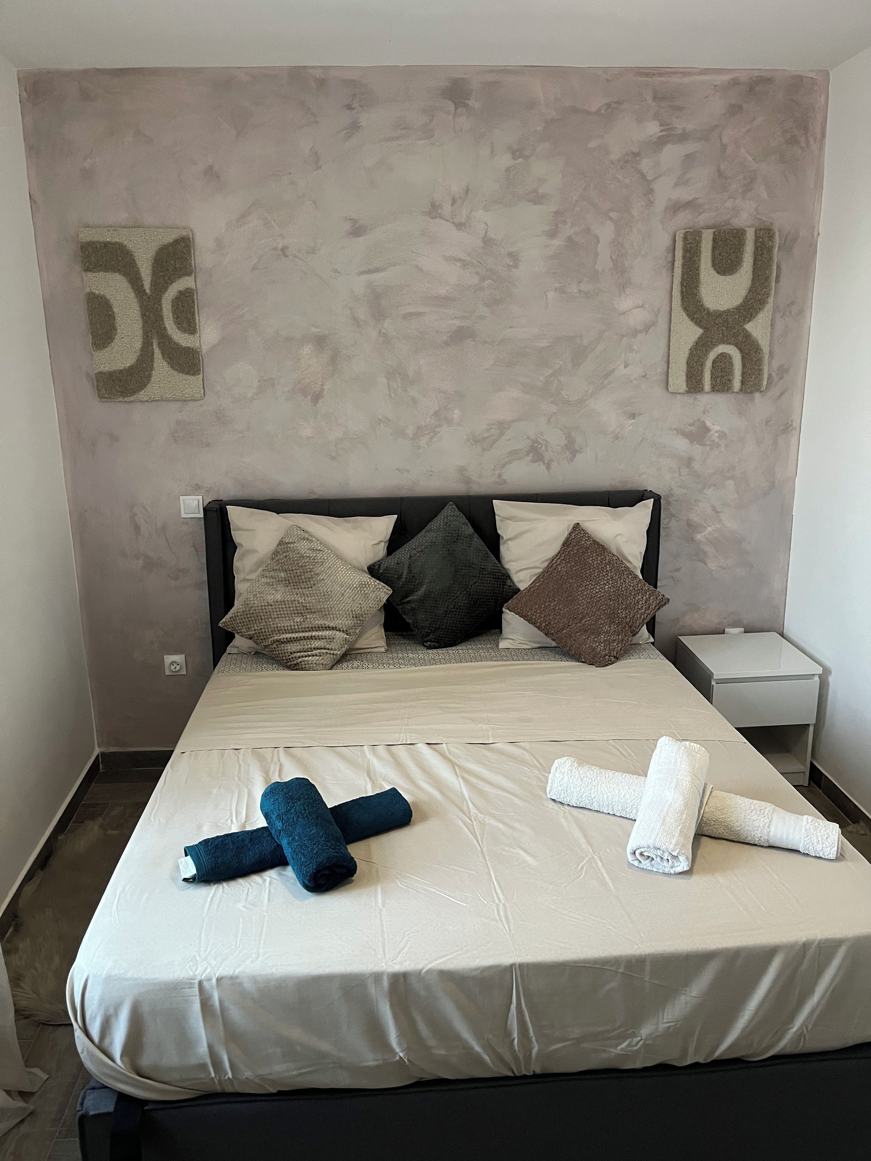 A hotel room with a bed, pillows, a nightstand, and towels.