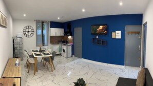 A modern kitchen with a built-in oven, a dining area with a table and chairs, and a living space with a sofa and a TV. - Elegant and cozy; apparently recently renovated (Béziers)