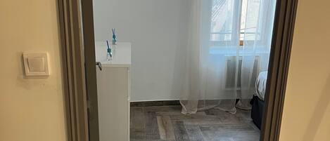 Une pièce dotée d’un parquet à motifs en chevrons, d’une armoire blanche et d’une fenêtre ornée de rideaux légers.