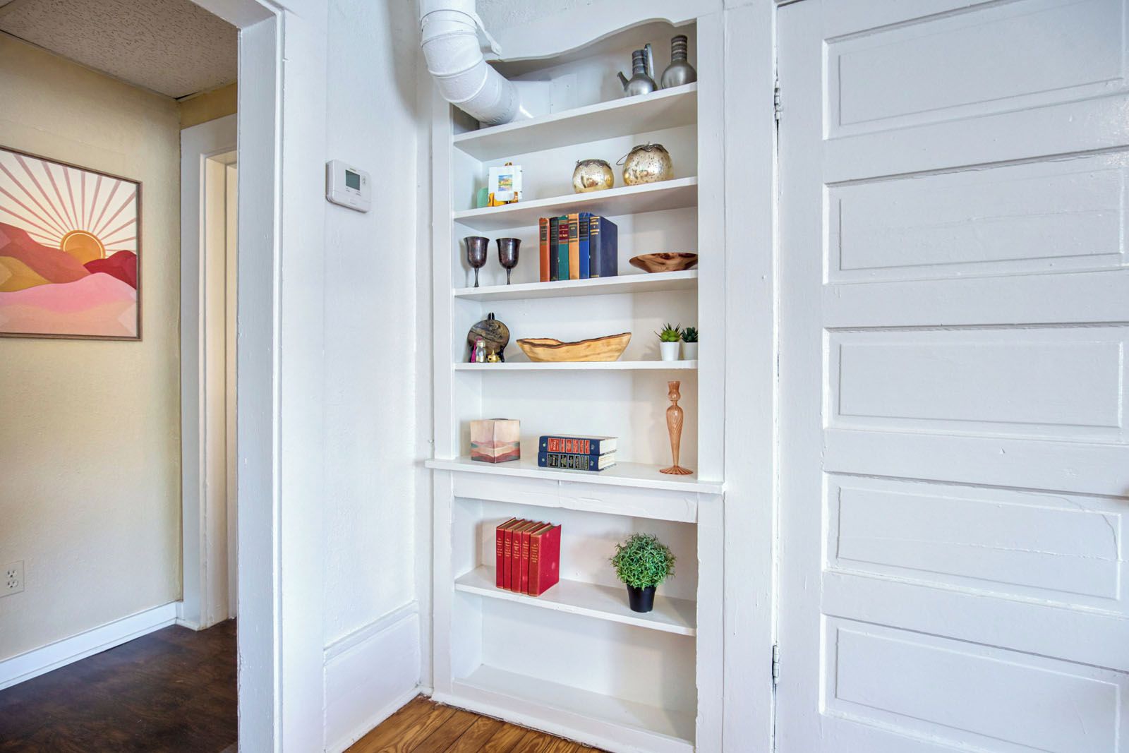 A white interior hallway with a built-in bookshelf, a thermostat, and a framed picture on the wall.