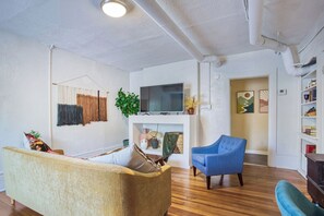 Ein Wohnzimmer mit einer Couch, einem blauen Sessel, einem Fernseher und einem Bücherregal.