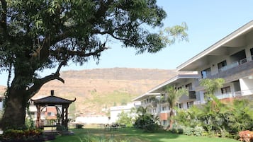 Een hotel met een grote boom, een pergola en uitzicht op een berg.