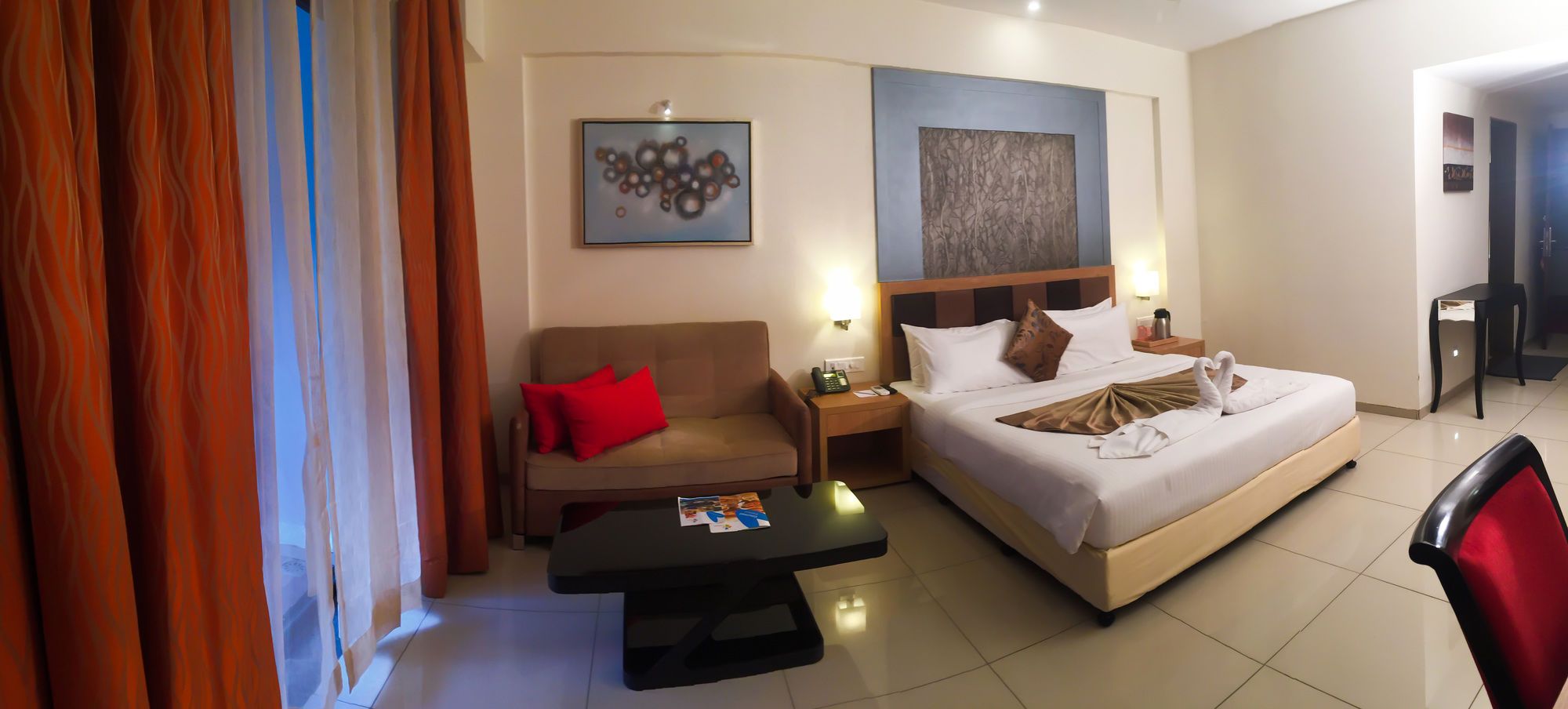 A hotel room with a bed, a sofa, a nightstand, a table, and a chair.
