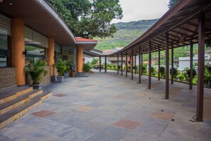 A covered outdoor area with stone flooring, columns, and potted plants. - Club Mahindra Hatgad (Surgana)
