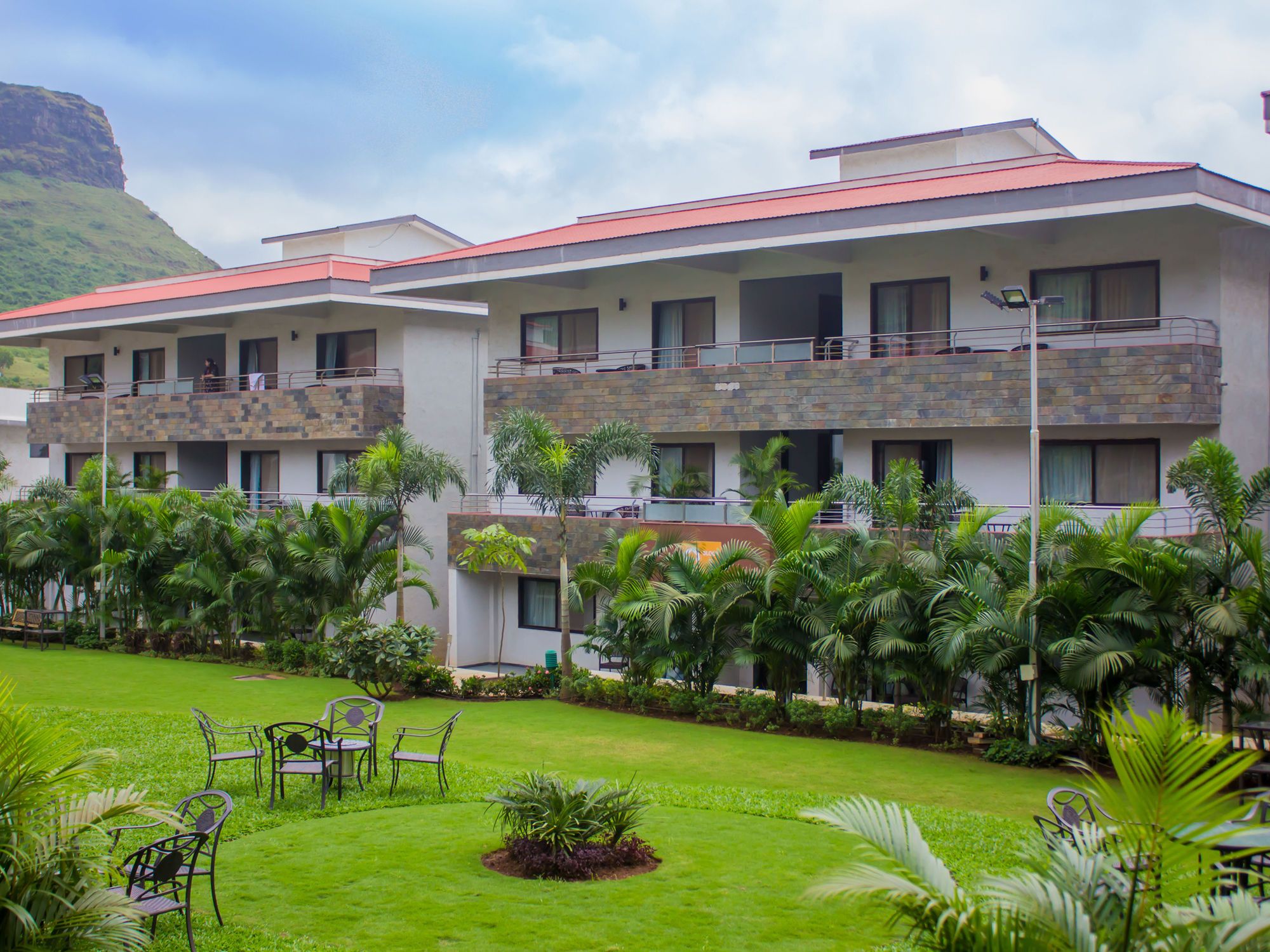 A hotel with multiple balconies, lush greenery, and a mountainous backdrop.
