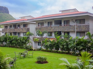 A hotel with multiple balconies, lush greenery, and a mountainous backdrop.