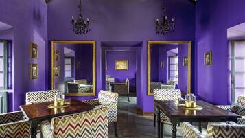 A room with purple walls, mirrored furniture, and chandeliers.