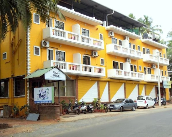 A multi-story yellow building with balconies, a sign for 'Viva Baga,' and parked cars.