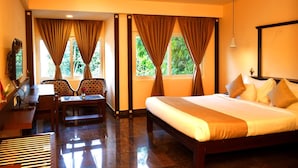 A hotel room with a bed, a desk with a chair, and a window with curtains. - DNC Shevaroys Resorts & Spa (Yercaud)