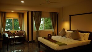 A hotel room with a bed, a desk, a chair, and a window with curtains. - DNC Shevaroys Resorts & Spa (Yercaud)