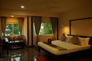 Quarto de hotel com cama, escrivaninha, cadeira e janela com cortinas.
