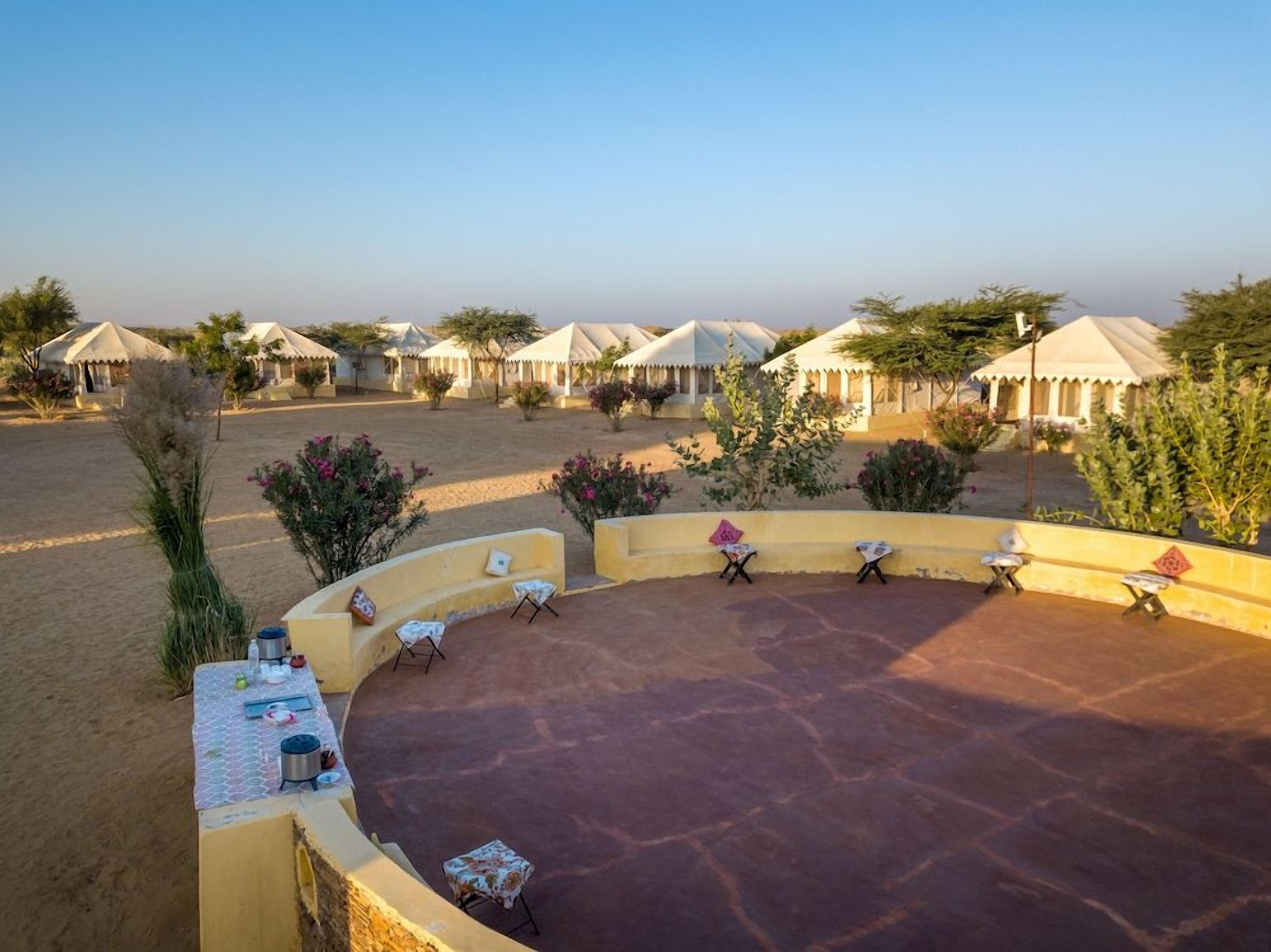 A desert resort with multiple tents, outdoor seating, and sparse vegetation.