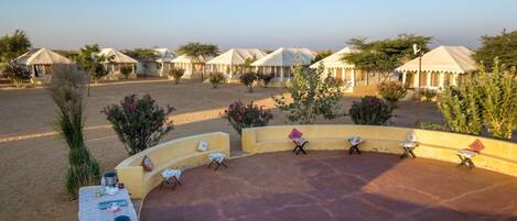A desert resort with multiple tents, outdoor seating, and sparse vegetation.