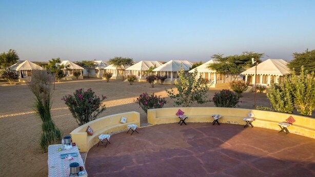Un resort en el desierto con varias tiendas de campaña y un área central de estar con mesas y sillas.
