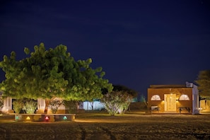 A building with a large tree in front, a well-lit entrance, and a pathway leading to the building. - Wind Desert Camp (Jaisalmer)