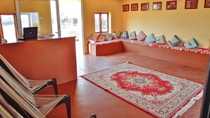 Una habitación con alfombra roja, un banco con cojines, una computadora portátil sobre una mesa y un techo con diseño.