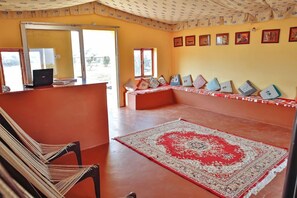 A room with a red carpet, a bench with cushions, a laptop on a table, and a patterned ceiling. - Wind Desert Camp (Jaisalmer)