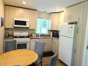 A compact kitchen with a microwave, stove, oven, and refrigerator. There is a dining table with chairs and a window providing natural light.