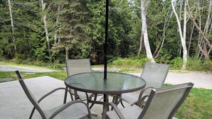 A round glass table with metal chairs in an outdoor setting with trees in the background. - Blacktail Cabin: Hot Tub, Playground, BBQ, Trails (Halfmoon Bay)