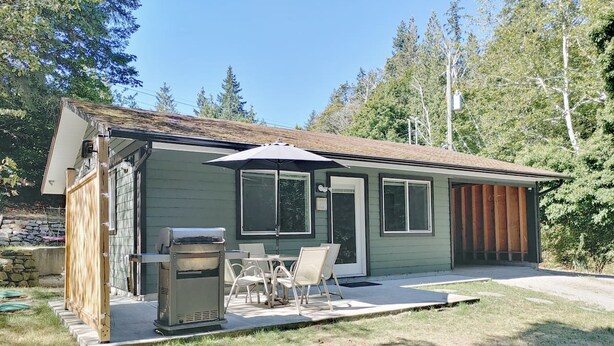A single-story house with a patio area, a grill, and a small deck. - Blacktail Cabin: Hot Tub, Playground, BBQ, Trails (Halfmoon Bay)