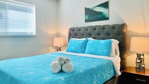 A bedroom with a bed, a nightstand, a lamp, and a wall-mounted painting. - Blacktail Cabin: Hot Tub, Playground, BBQ, Trails (Halfmoon Bay)