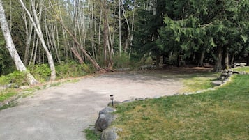 Un chemin de gravier mène à une zone abritée, où se trouve un lampadaire, le tout étant entouré d’arbres et de rochers.