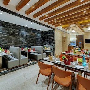 A modern restaurant interior with high ceilings, wooden beams, and marble walls. Tables are set with chairs, and the space is well-lit. - Treebo Metropolis (Mumbai)