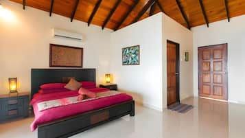 A bedroom with a bed, nightstands, an air conditioning unit, a door, and a wall-mounted artwork.