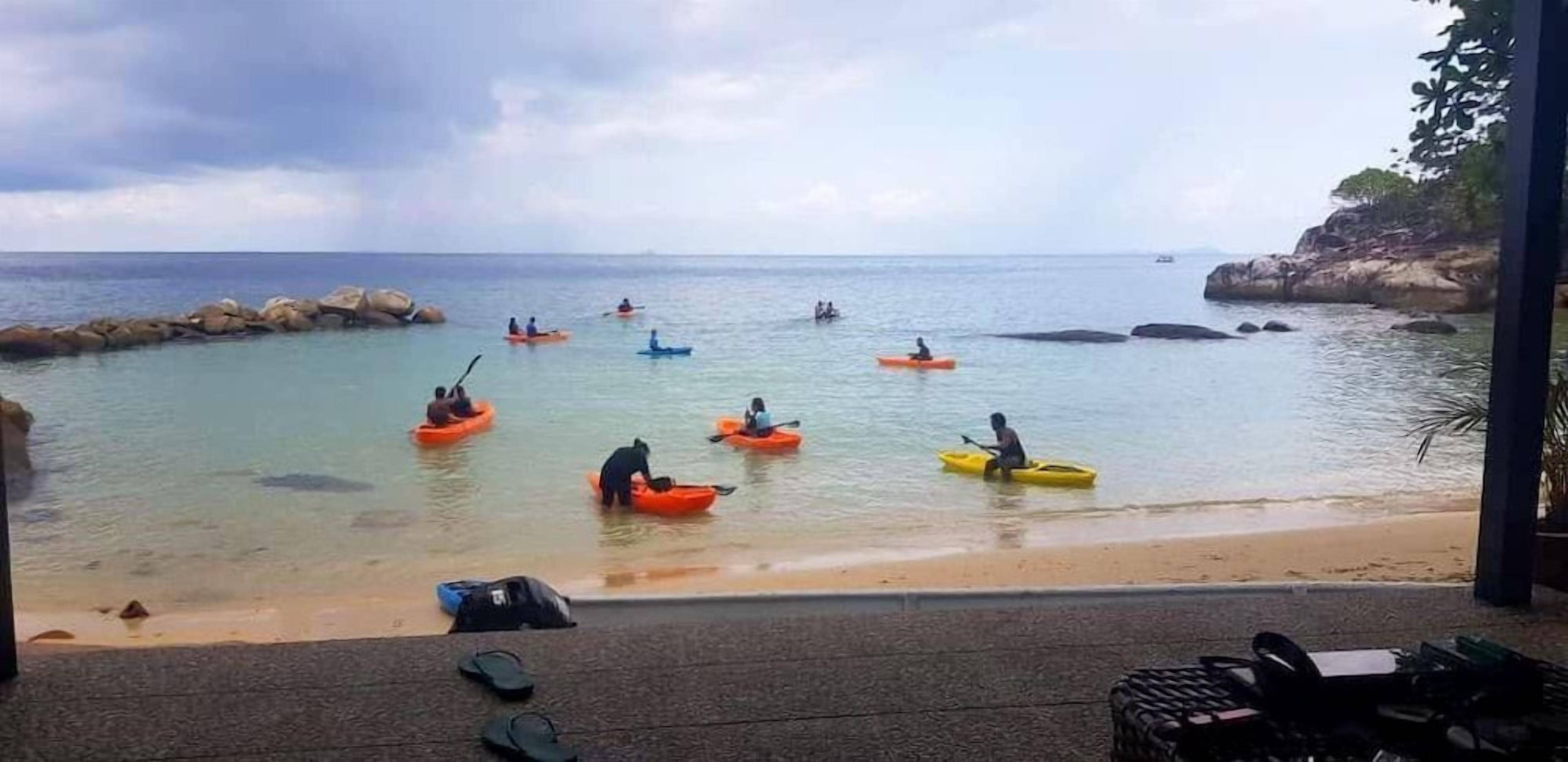 A beach with kayaks and people paddling, a rocky shoreline, and a clear view of the sea.