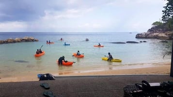 A beach with kayaks and people paddling, a rocky shoreline, and a clear view of the sea.