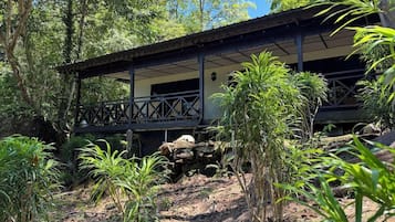 A rustic building with a balcony, surrounded by lush greenery and trees.