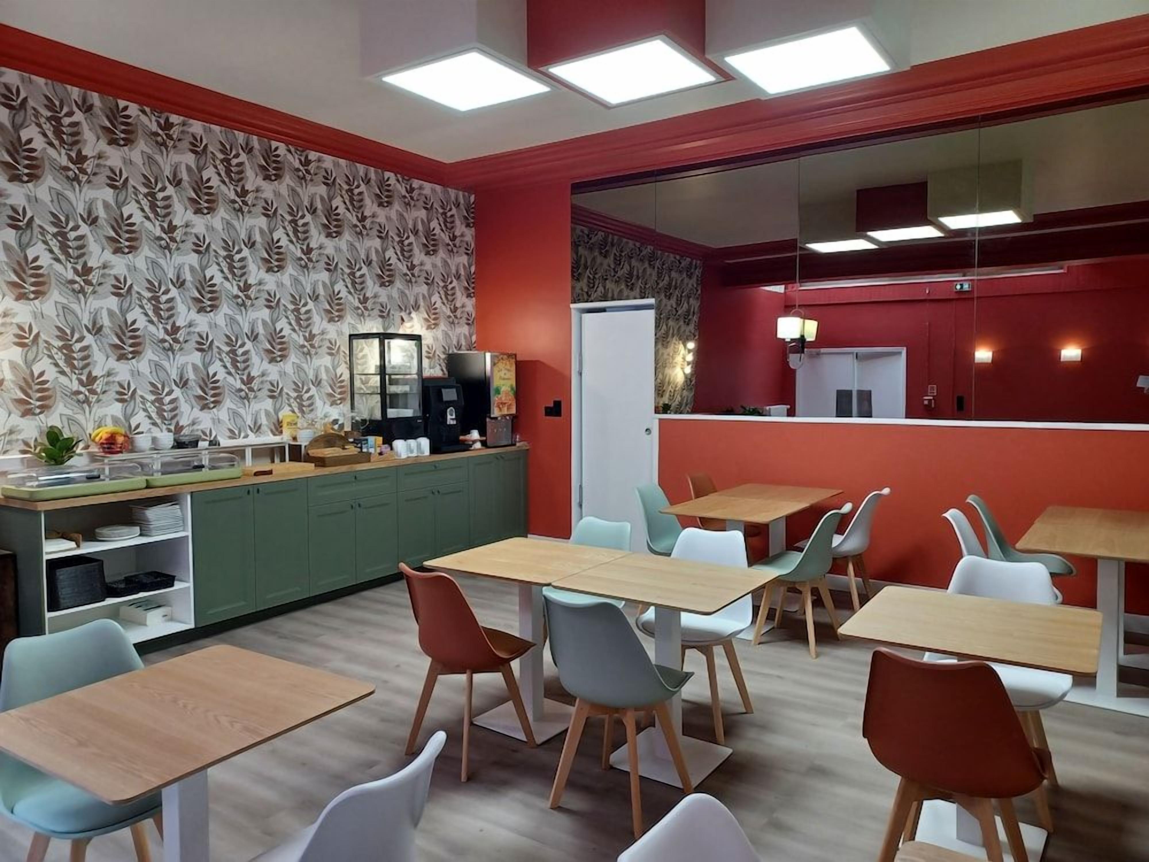 Un espace repas moderne avec plusieurs tables et chaises, un coin cuisine doté d’un comptoir et un mur orné d’un motif.