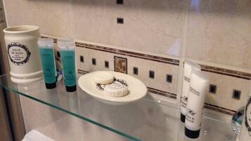 A bathroom with a glass shelf holding toiletries, a white sink, and a marble wall with a decorative border.